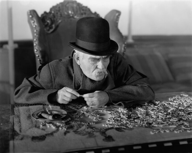 A historical photo of an elderly man solving a jigsaw puzzle