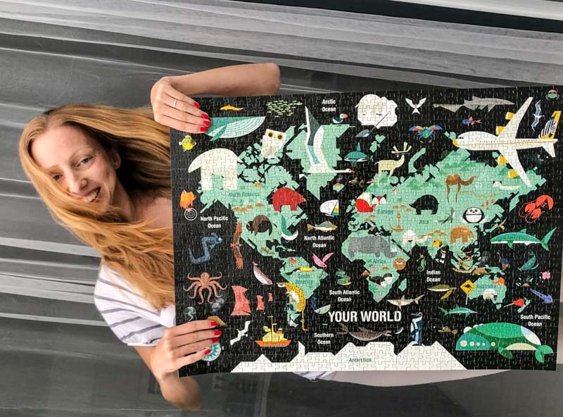 Veronika of Jigsaw Puzzle Queen holding a finished puzzle depicting a creative world map